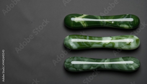 Set of three green marble gua sha massage tools on dark gray background, flat lay wellness concept for skincare and natural beauty rituals