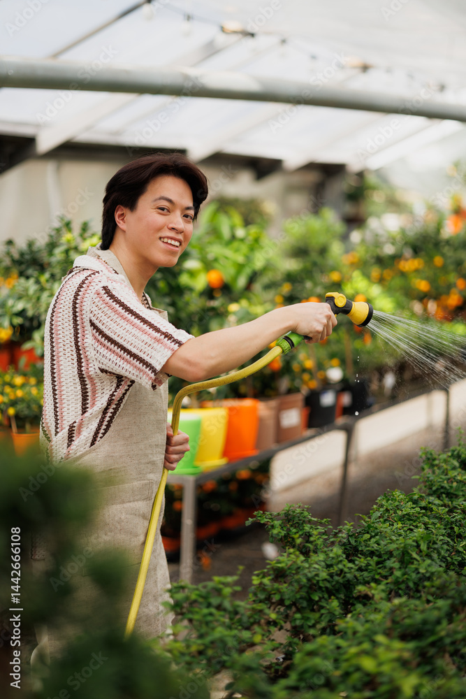 Asian florist smiling and looking at camera while watering bonsai trees Asian florist smiling and looking at camera while watering bonsai trees