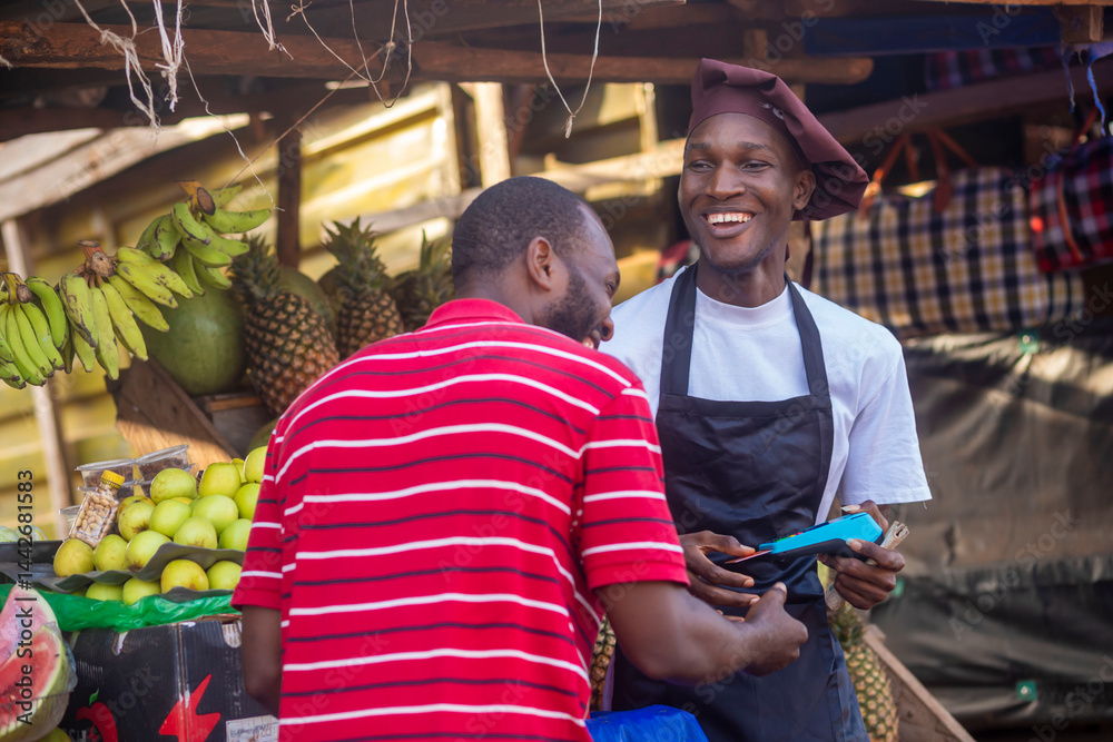 Obraz premium Person paying for fruits with a credit card while african fruit seller holding an electronic POS machine