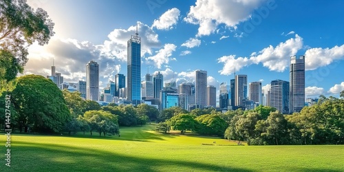 Lush park grass with city skyline under blue sky and clouds.