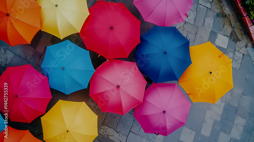 Colorful umbrellas in vibrant red, blue, yellow, pink, and orange shades create lively overhead view on stone pavement, evoking cheerful and artistic atmosphere