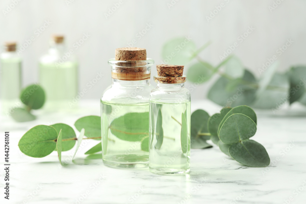 Bottles of essential oil and eucalyptus leaves on white marble table Bottles of essential oil and eucalyptus leaves on white marble table