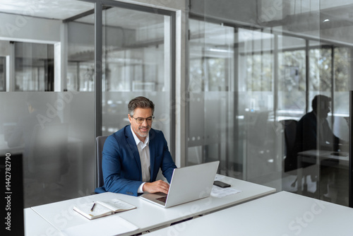 Smiling senior businessman entrepreneur sitting at desk working on financial project, looking thinking at screen. Mature 50s Latin business man ceo manager using laptop computer in office. Copy space