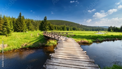 wooden bridge over izera river and green meadows with spruce trees on hala izerska on sunny spring day jizera mountains lower silesia poland