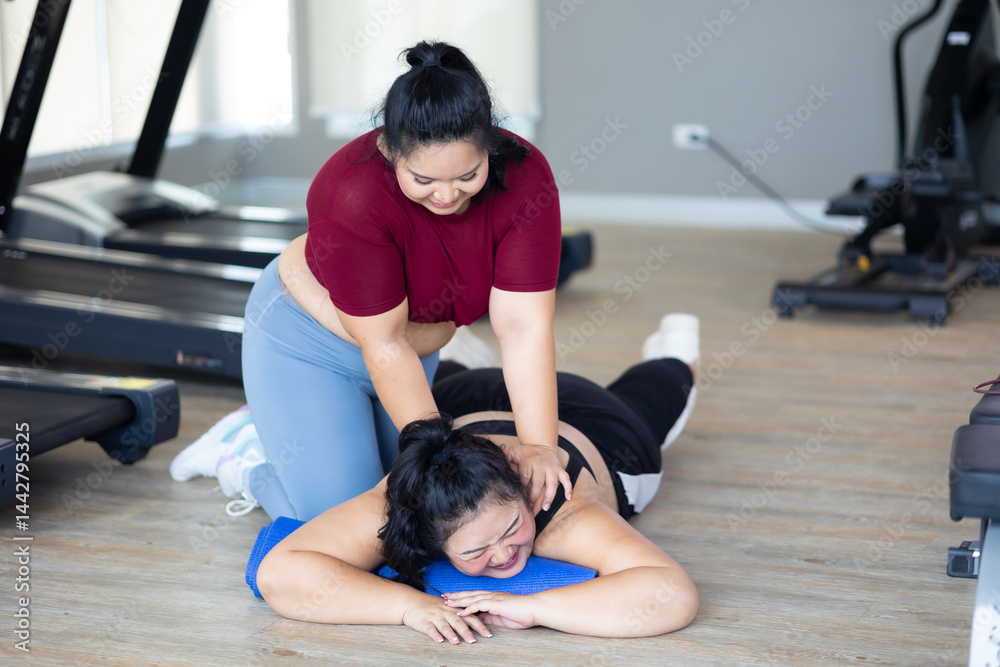 Friends back massage. beautiful young chubby overweight woman wearing sporty fitness clothes doing exercise indoors at gym fitness sport club, body and health care