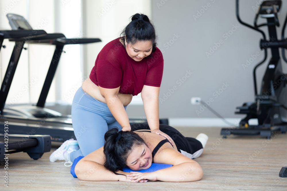 Friends back massage. beautiful young chubby overweight woman wearing sporty fitness clothes doing exercise indoors at gym fitness sport club, body and health care