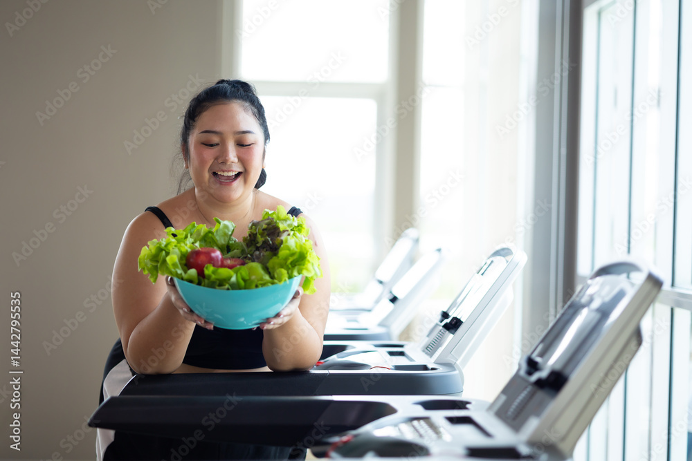 Portrait fat woman enjoying eating vegetable salad. beautiful young chubby overweight woman wearing sporty fitness clothes doing exercise indoors at gym fitness sport club, body and health care
