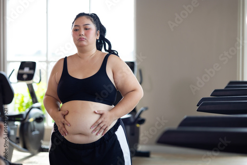 Obraz na płótnie Portrait woman and fat belly. beautiful young chubby overweight woman wearing sporty fitness clothes doing exercise indoors at gym fitness sport club, body and health care w salonie
