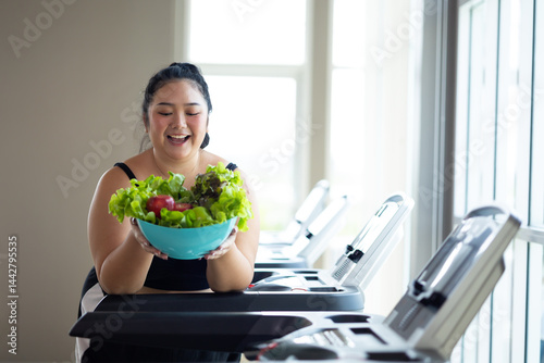 Obraz na płótnie Portrait fat woman enjoying eating vegetable salad. beautiful young chubby overweight woman wearing sporty fitness clothes doing exercise indoors at gym fitness sport club, body and health care w salonie