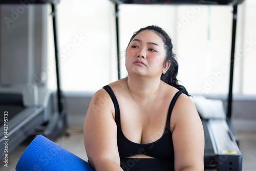 Obraz na płótnie Tired fat asian woman. beautiful young chubby overweight woman wearing sporty fitness clothes doing exercise indoors at gym fitness sport club, body and health care w salonie