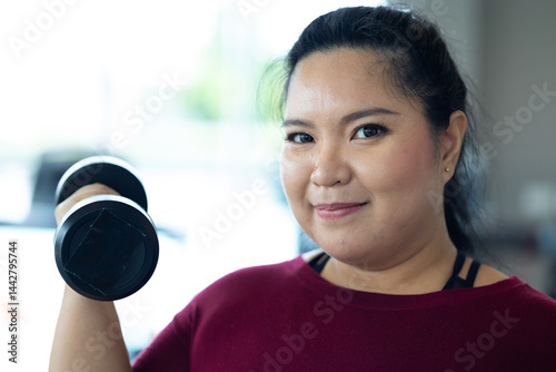 Obraz na płótnie Young woman exercising with dumbbells. beautiful young chubby overweight woman wearing sporty fitness clothes doing exercise indoors at gym fitness sport club, body and health care w salonie