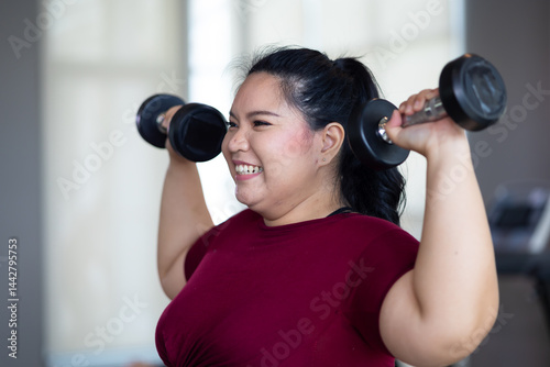 Obraz na płótnie Young woman exercising with dumbbells. beautiful young chubby overweight woman wearing sporty fitness clothes doing exercise indoors at gym fitness sport club, body and health care w salonie