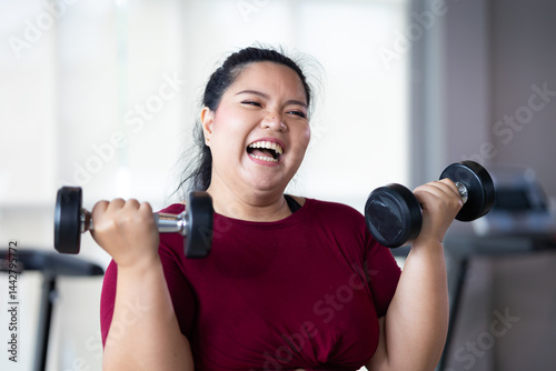 Young woman exercising with dumbbells. beautiful young chubby overweight woman wearing sporty fitness clothes doing exercise indoors at gym fitness sport club, body and health care