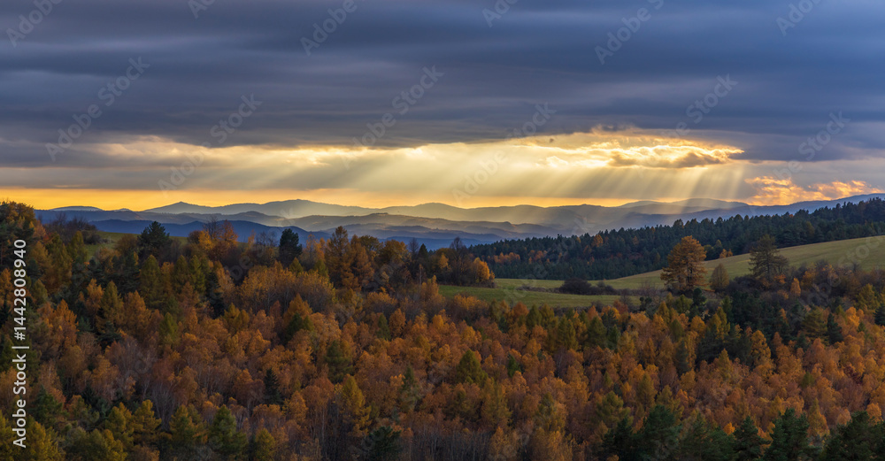 Sun rays shining through clouds over colorful autumn forest landscape with Low Tatras