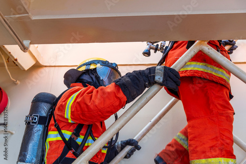A firefighters climbing the stairs in full protective gear, mask, and oxygen tank stands ready during a fire drill on board. Fully equipped, he executes fire suppression tasks with required precision.