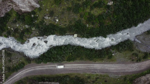 Top view of the seething mountain river and the road, in the lowland between the sheer cliffs, with a car moving along it