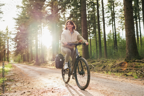 Wellness in motion, a vibrant woman pedals her way through a peaceful forest retreat at sunset