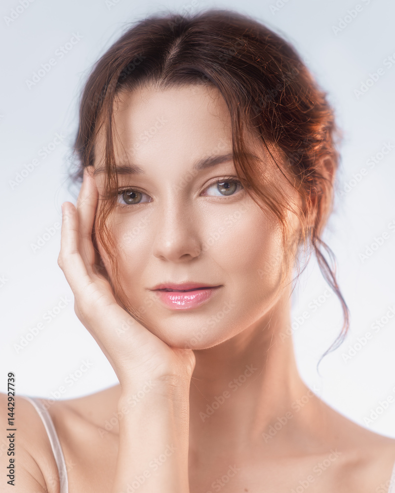 Elegant close-up of a young Caucasian woman with flawless glowing skin and glossy lips gently touching her face. Ideal for skincare, cosmetic ads, natural beauty, and wellness visuals.