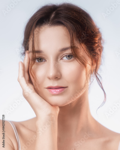 Obraz na płótnie Elegant close-up of a young Caucasian woman with flawless glowing skin and glossy lips gently touching her face. Ideal for skincare, cosmetic ads, natural beauty, and wellness visuals. w salonie