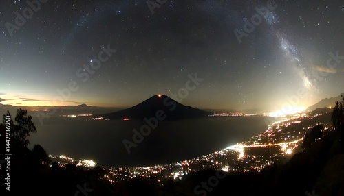 Majestic volcano silhouetted against a breathtaking night sky, studded with stars and the Milky Way, overlooking a city glowing with lights below. photo