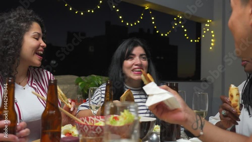 Smiling young Latin woman speaks, holding food, at a gathering with friends in the evening