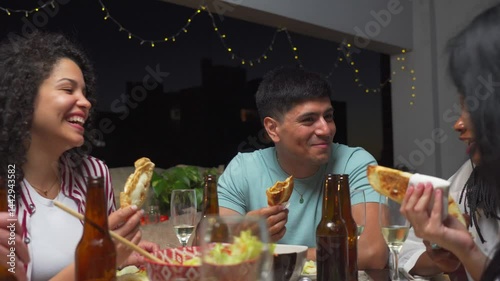 Young Latin friends enjoy a fun evening dinner on a rooftop terrace with traditional Argentinean food