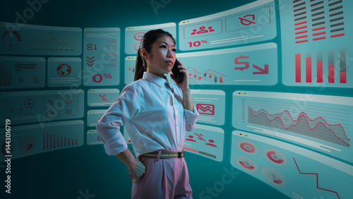 Businesswoman discusses business data trends via phone call, surrounded by multiple digital graphic displays showing declining charts. Concept of business, graphics, digital economy, trends, crisis