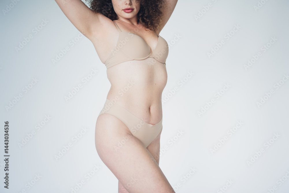 Portrait of a confident young woman with curly hair wearing nude lingerie on a white background showing natural beauty and self acceptance