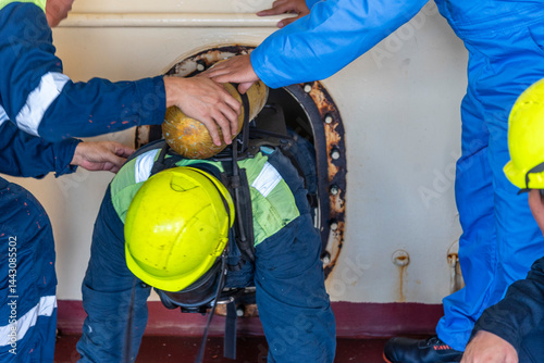 Foto Crew member wearing breathing apparatus exits a narrow hatch after providing first aid during a man evacuation drill from a confined space on a merchant ship