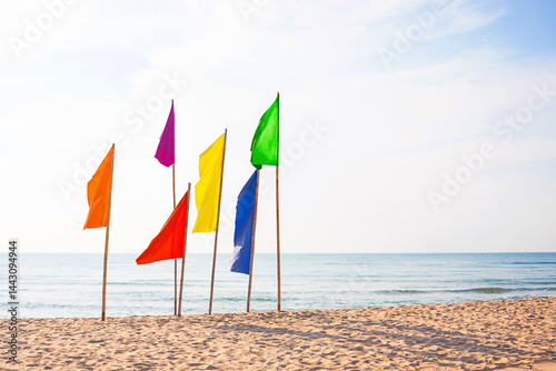 Lgbt concepts with serene beach scene featuring a row of vibrant flags in various colors fluttering in the breeze, set against a calm sea and blue sky