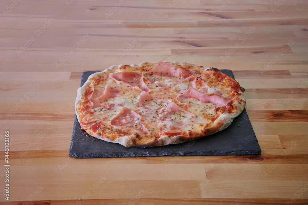 A pizza with ham and cheese on a wooden table. The pizza is cut into slices. There are no other objects in the image