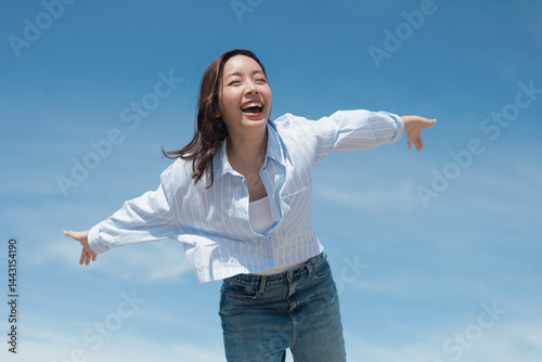 A cheerful woman wearing a casual shirt and jeans standing in front of the blue sky background with copy space.