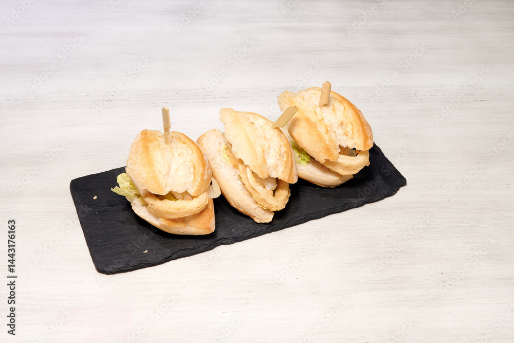 Three sandwiches on a black plate. The sandwiches are cut in half and have toothpicks in them