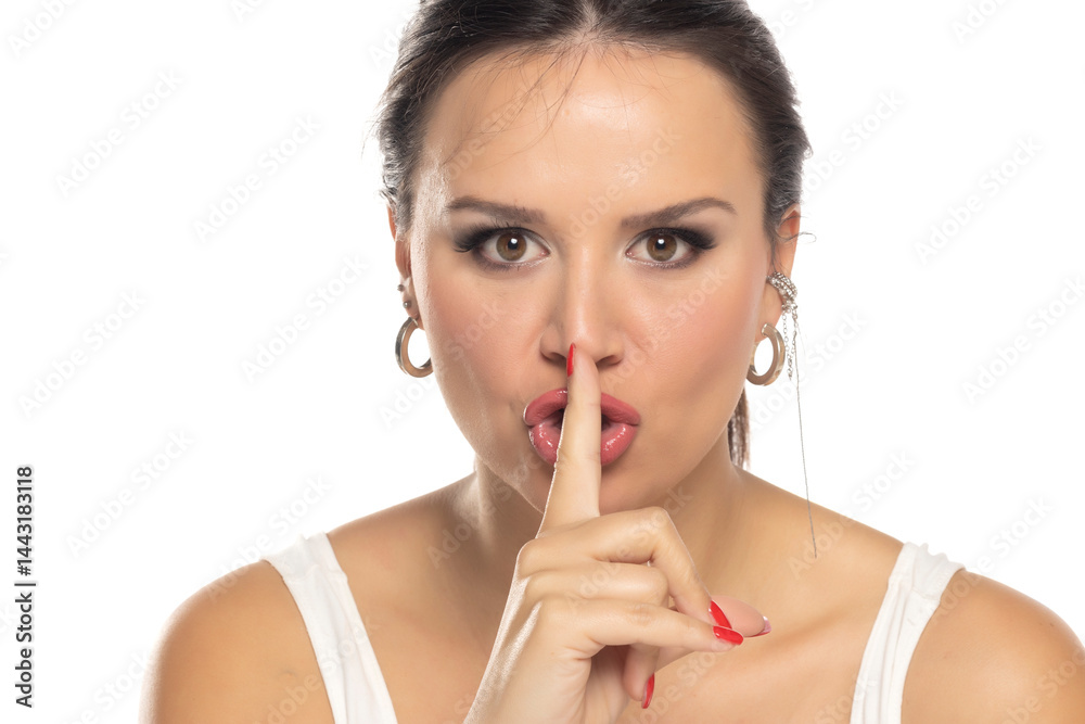 Woman in white tank top making shushing gesture with finger on lips. Serious expression, direct gaze. Signaling for silence or secrecy. Studio portrait on white background Woman in white tank top making shushing gesture with finger on lips. Serious expression, direct gaze. Signaling for silence or secrecy. Studio portrait on white background