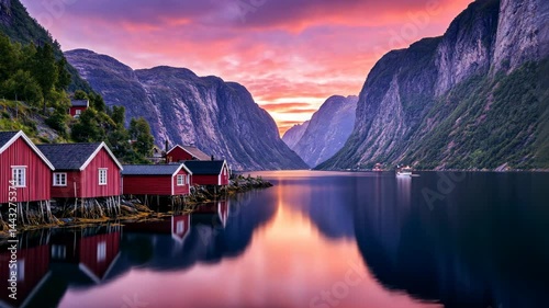 Lakeside cabin glowing at sunset, reflected on calm fjord waters.

