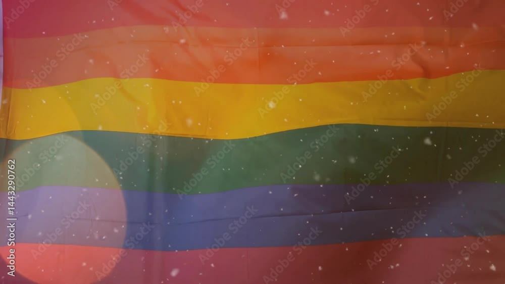 Rainbow pride flag fabric unfolding in close-up view, showing confetti flecks and lens-flare glow