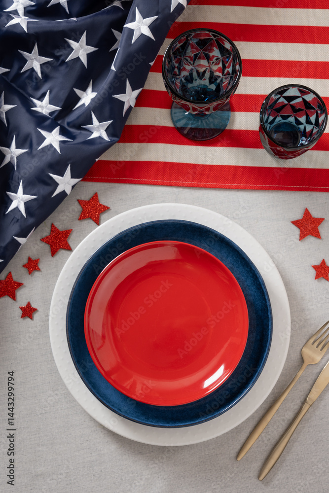 Table setting for USA Independence Day. Festive dinner with empty red plate and decoration in USA national flag colors and stars. Copy space. Vertical. View from above