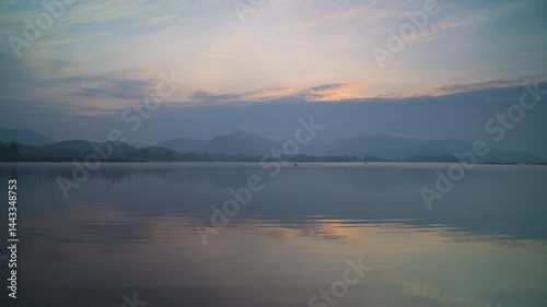 A calm lake with a beautiful sunset in the background. The sky is filled with clouds, creating a serene and peaceful atmosphere