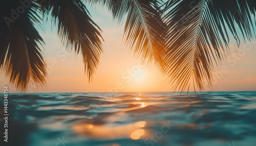 Tropical sunset over ocean waves. Lush palm leaves frame the vibrant sunset colors on the horizon.  Peaceful, serene scene