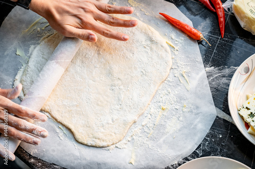 Obraz na płótnie Making homemade pizza with three types of cheese - women's hands in action. Close-up scene of women's hands rolling out homemade pizza dough on a kitchen countertop. w salonie