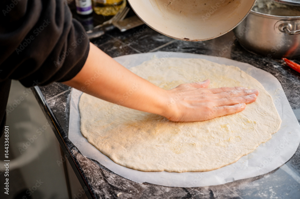 Close-up scene of female hands applying white sauce to dough on kitchen countertop. Making homemade pizza with three types of cheese - female hands in action.