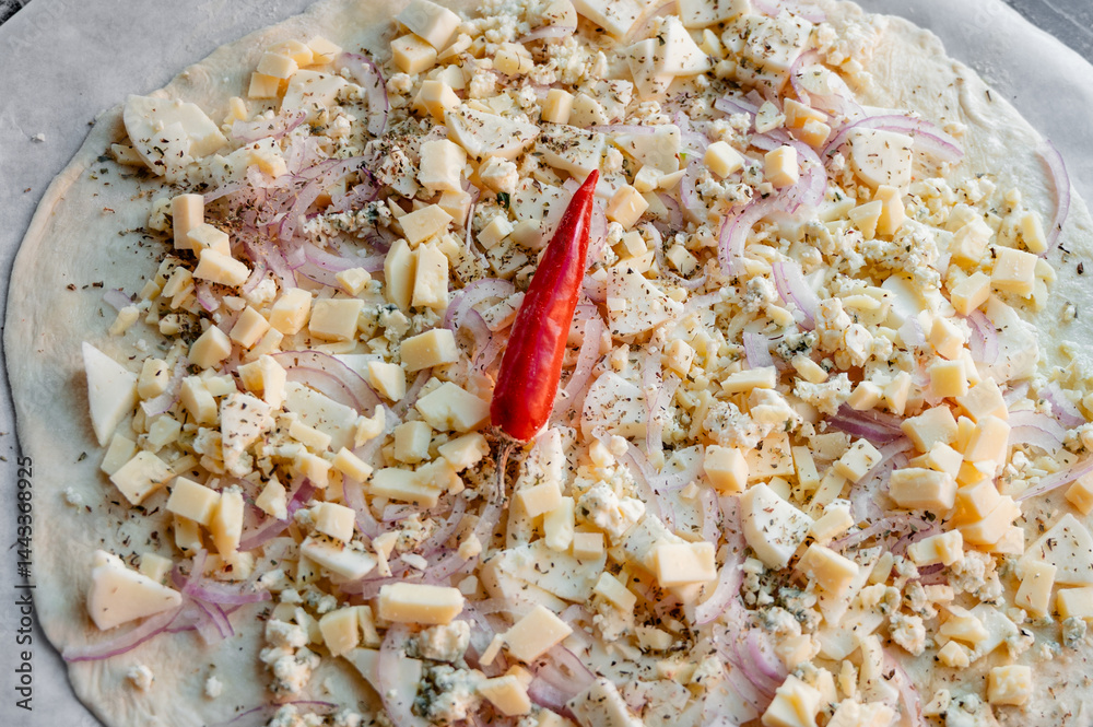 A homemade pizza in its raw form, assembled with toppings. The dough is uncooked but fully prepared with sauce, cheese, and fresh ingredients. The kitchen is cozy and softly lit, with utensils, bowls,