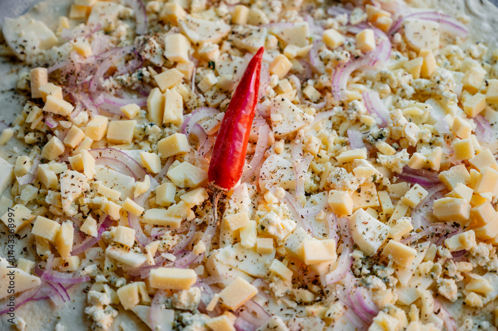 A homemade pizza in its raw form, assembled with toppings. The dough is uncooked but fully prepared with sauce, cheese, and fresh ingredients. The kitchen is cozy and softly lit, with utensils, bowls,