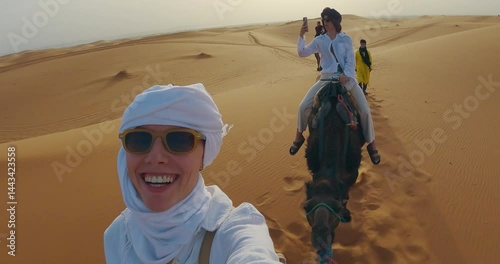 Group of individuals rides camels in a desert environment during a safari tour