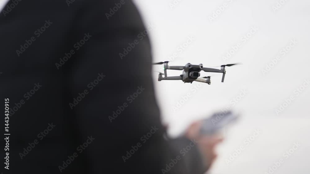 Operator bringing back the drone using controller on flight above mountain lake and forest, slow motion