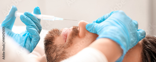 Closeup of plastic surgeon making nonsurgical rhinoplasty for middle aged rich man at aesthetic clinic, injecting filler in his nose, side view. Modern aesthetic medicine and cosmetology concept