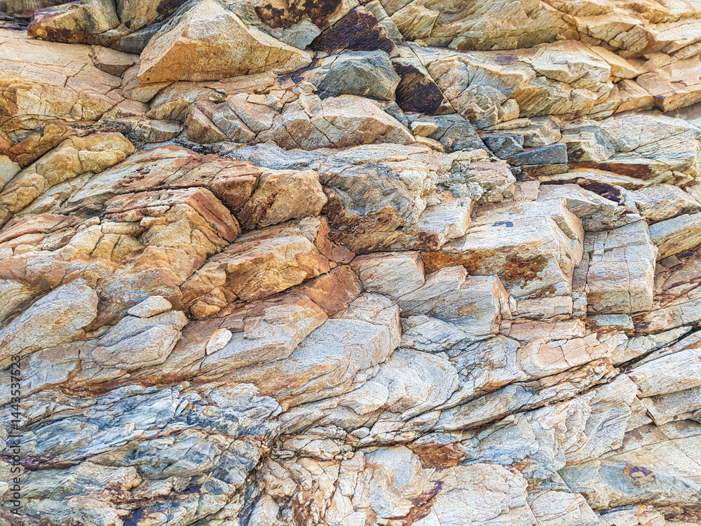 Unique rock formations display a blend of earthy tones and textures under bright sunlight. The natural beauty showcases layers of minerals and geological history, inviting exploration