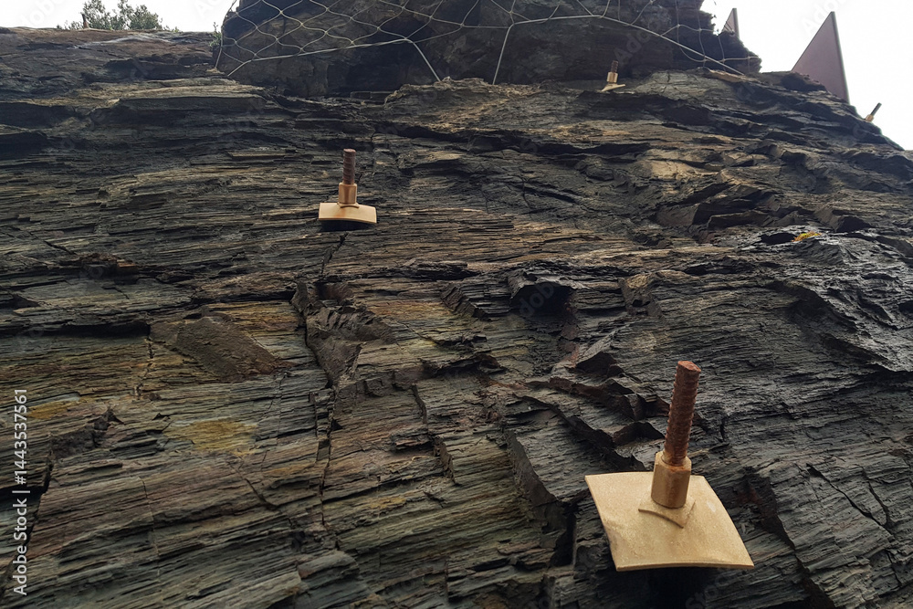 Climbers prepare for a competition on a natural rock face featuring wooden climbing holds. The setting showcases rugged cliffs and a dramatic sky during late afternoon