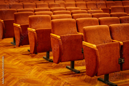 Rows of plush orange seats in an empty auditorium, set on a polished wooden floor with warm lighting and rich ambiance. Great for presentations and performances.