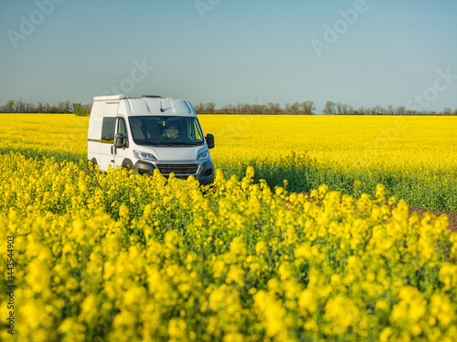 view to white camper van through a lot of blooming rapeseed flowers in spring day with copy space